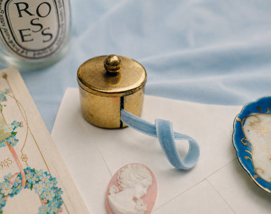 Vintage brass postage stamp roll holder with warm aged patina surrounded by vintage post cards an envelope and candle