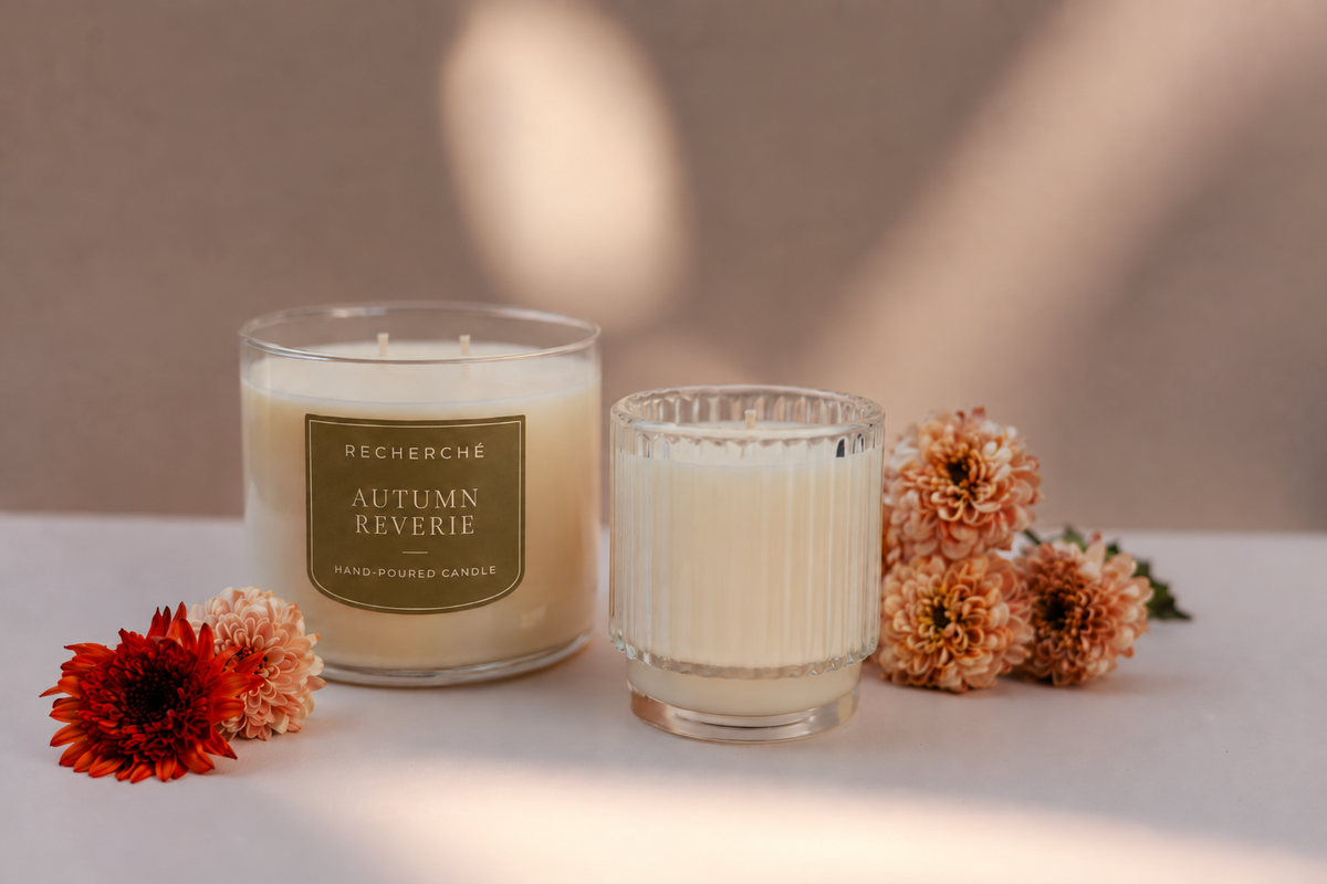 Two hand poured candles by recherché on a tabletop surrounded by fall flowers 