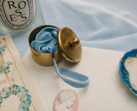 Vintage brass postage stamp roll holder with warm aged patina surrounded by vintage post cards an envelope and candle