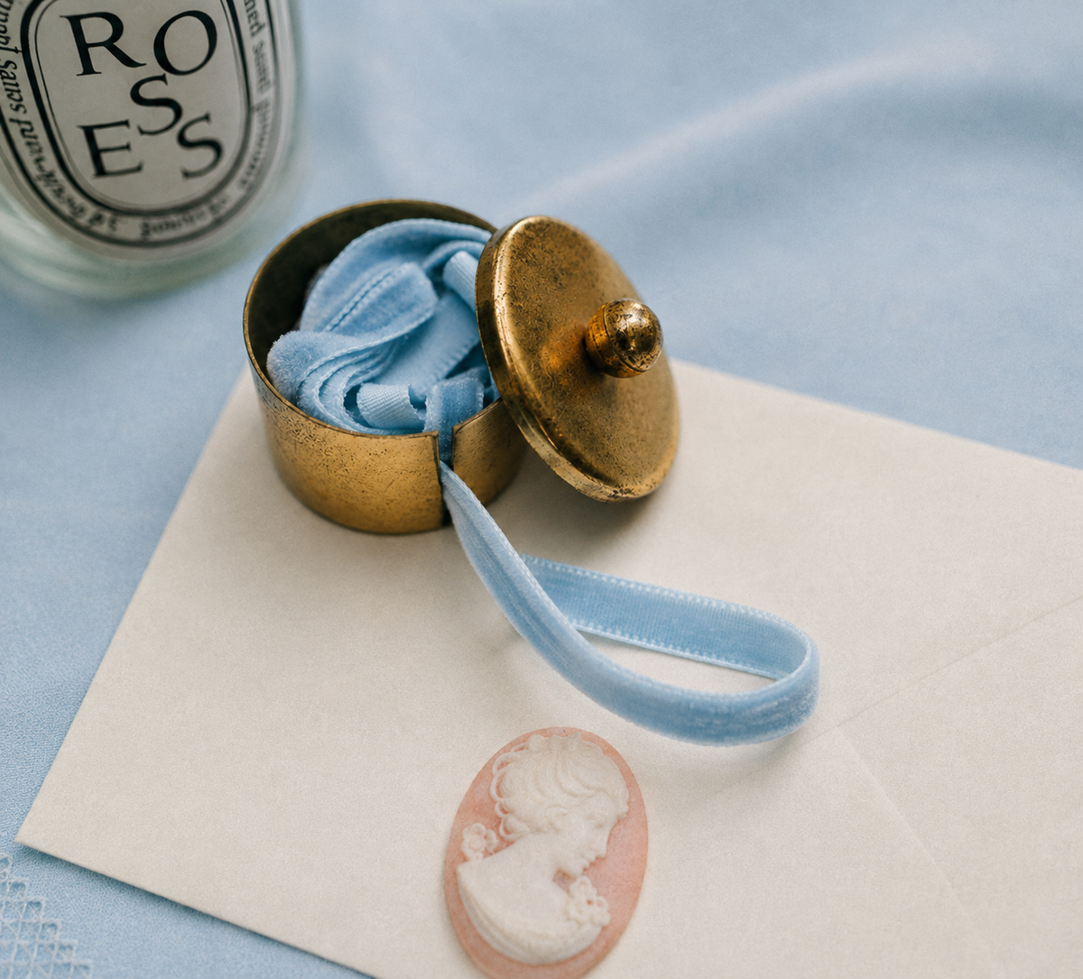 Vintage brass postage stamp roll holder with warm aged patina surrounded by vintage post cards an envelope and candle